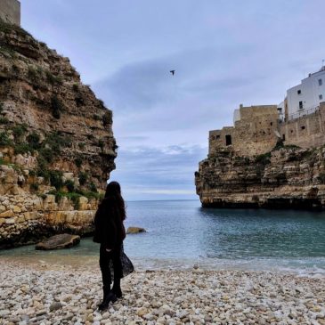 Widok z mostu na pustą plażę Lama Monachile w Polignano a Mare zimą; turkusowa woda Adriatyku uderzająca o białe skały.