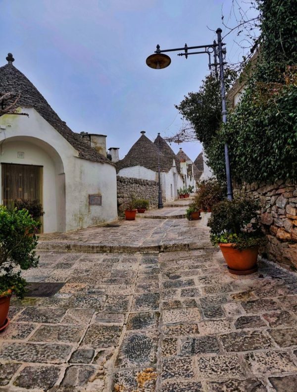 Panoramiczny widok na dachy domków trulli w dzielnicy Rione Monti w Alberobello; charakterystyczne stożkowe dachy z symbolami malowanymi wapnem pod błękitnym niebem w lutym.